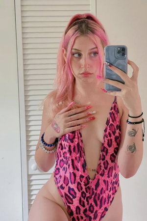 Pink-haired woman in leopard bodysuit taking mirror selfie.