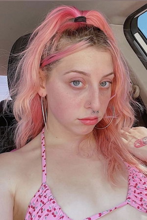Woman with pink hair in cherry top taking car selfie.
