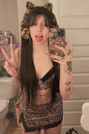 Dark-haired woman in leopard print outfit taking bathroom mirror selfie.