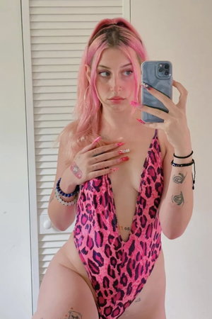 Pink-haired woman in leopard swimsuit taking mirror selfie indoors.