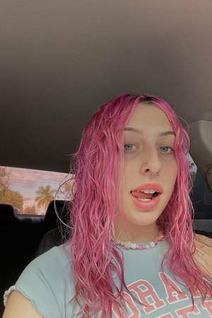 Woman with pink hair in t-shirt inside car.