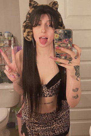 Woman with long dark hair in leopard print outfit and cat ears, taking mirror selfie in bathroom.