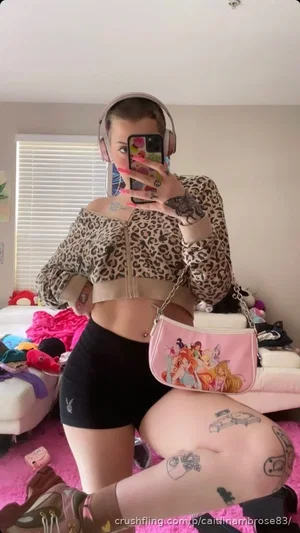 Woman in leopard crop top and black shorts, tattoos, pink rug, mirror selfie.