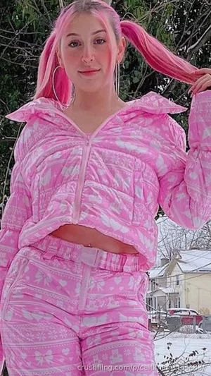 Woman with pink hair in pigtails, wearing pink patterned cropped jacket and pants, outdoors in