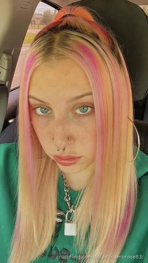 Woman with pastel pink and blonde hair, wearing green hoodie, sitting in car.