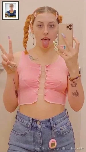 Woman with braided hair in pink crop top and jeans, making peace sign and sticking out tongue in
