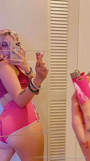 Woman in pink crop top and shorts takes mirror selfie, holding lighters, indoor setting.