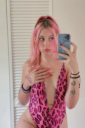 Woman with pink hair in pink leopard swimsuit, indoor selfie.