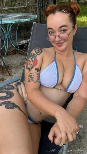 Woman with tattoos in blue bikini sitting outdoors on lounge chair.
