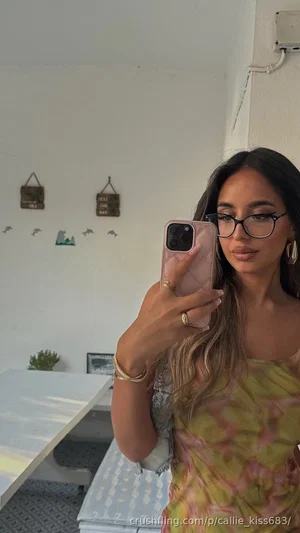 Woman with long dark hair and glasses takes mirror selfie in colorful strapless top, indoors.