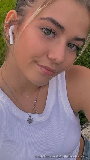 Woman with blonde hair in white tank top, outdoors on grass, smiling at camera.