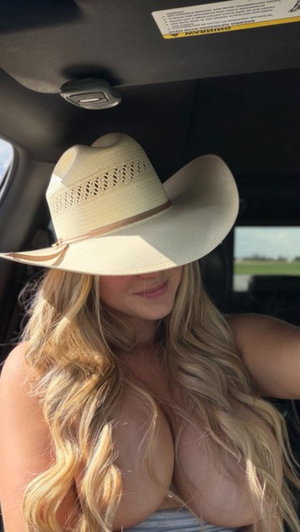Blonde woman in cowboy hat taking car selfie.