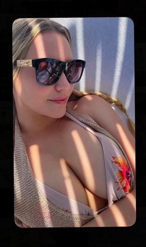 Blonde woman in bikini top and sunglasses outdoors.