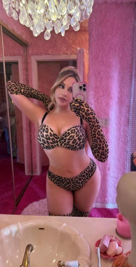 Woman in leopard print lingerie and gloves poses in pink bathroom mirror selfie.