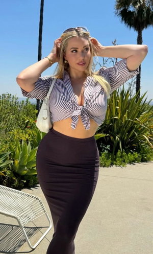 Blonde woman in striped crop top and dark skirt outdoors.
