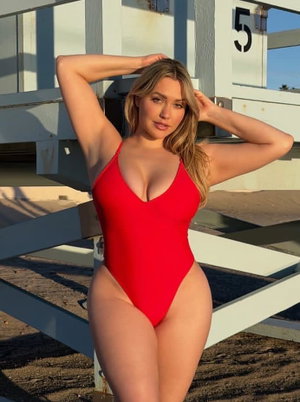 Blonde woman in red swimsuit posing outdoors near white structure.