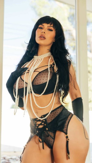 Woman in black lingerie with pearls posing indoors.