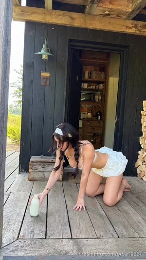 Woman in white top and shorts kneeling on wooden porch, reaching for bottle.