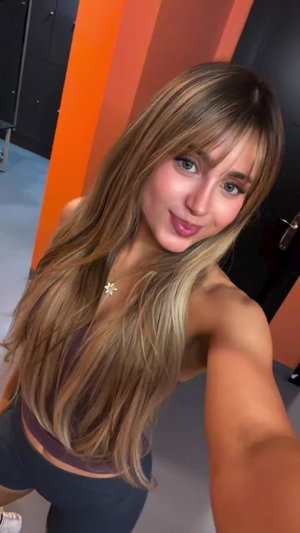 Woman with long blonde hair in a crop top and leggings, posing indoors.