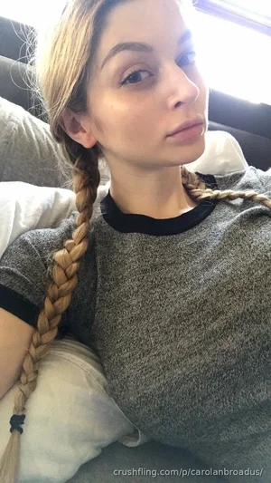 Woman with blonde braids wearing gray t-shirt, sitting on couch indoors.