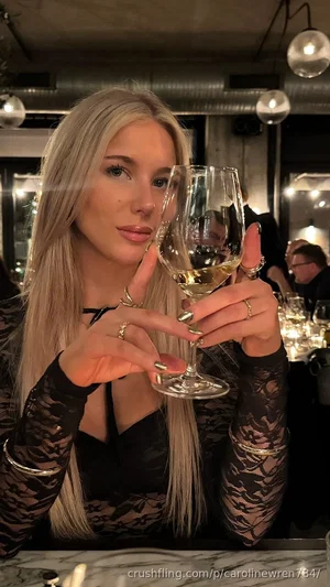 Woman with long blonde hair in black lace top holding wine glass at restaurant.