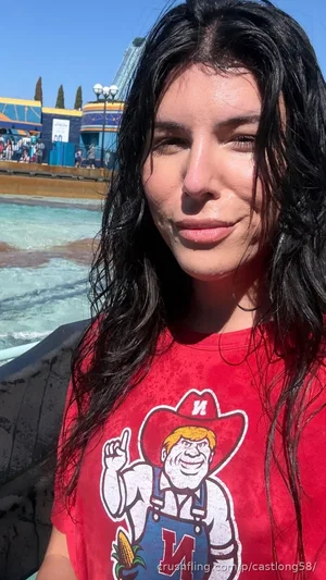 Woman with wet dark hair in red t-shirt at water park, smiling at camera.