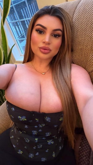 Woman with long brown hair in floral top taking indoor selfie.