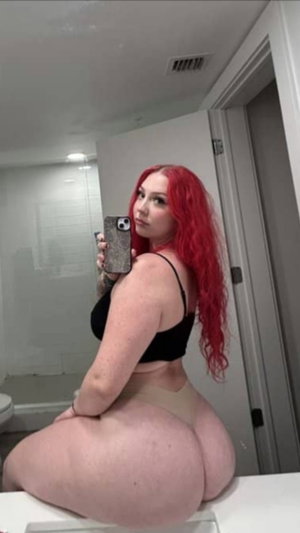 Redhead woman in black top and beige bottoms taking mirror selfie.