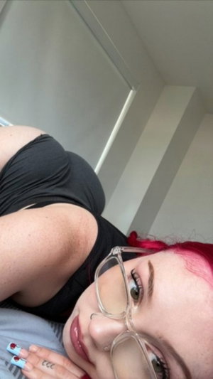 Woman with red hair and glasses lying down, wearing black top, indoors.