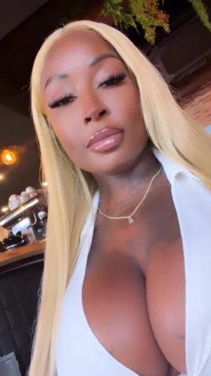 Woman with blonde hair and tattoos wears white top, indoors.