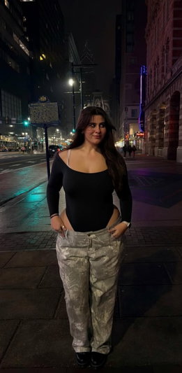 Woman in black top and patterned pants standing on city street at night.