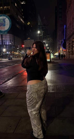 Woman in black crop top and camo pants posing on city street at night.