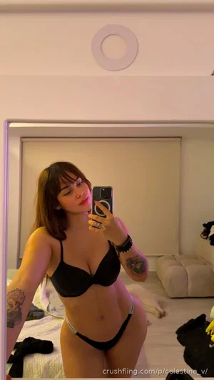 Woman in black lingerie taking mirror selfie in bedroom.
