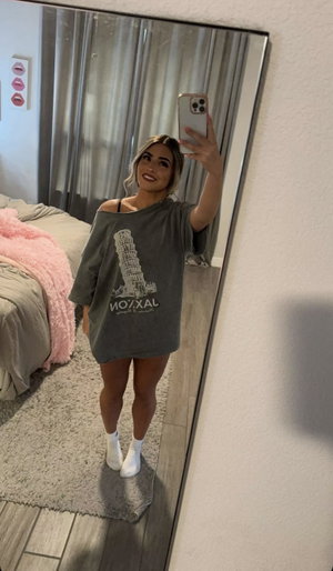 Woman in oversized gray t-shirt and white socks takes mirror selfie in bedroom.