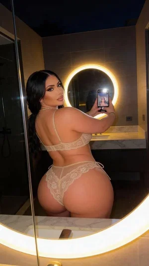 Woman in beige lace lingerie taking mirror selfie in bathroom.