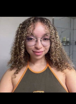 Woman with curly hair and glasses wearing a green tank top in a bathroom.