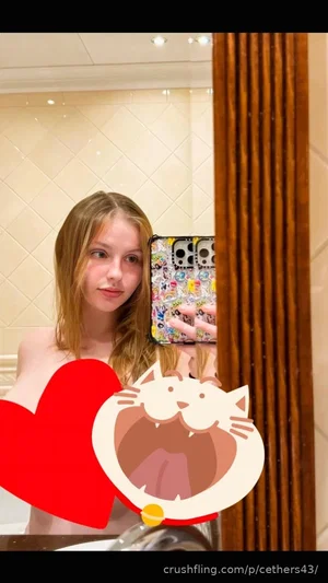 Woman with light hair in a bathroom mirror selfie, topless, holding phone with sticker cover.
