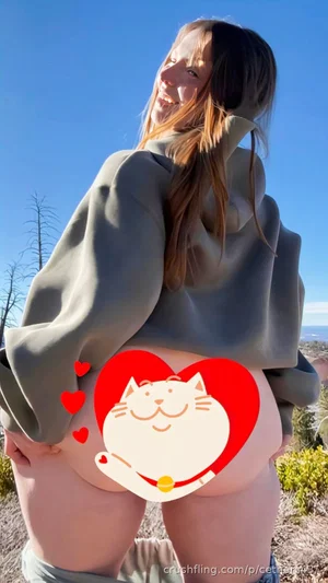 Woman in oversized hoodie and jeans, outdoors, showing bare buttocks with cartoon heart sticker.