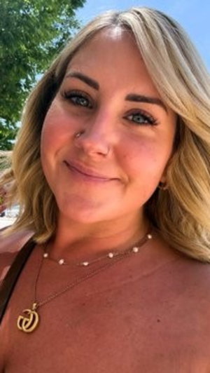 Blonde woman with necklaces taking outdoor selfie.