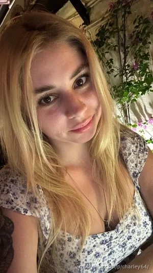 Blonde woman in floral top, smiling, indoor setting with plants.