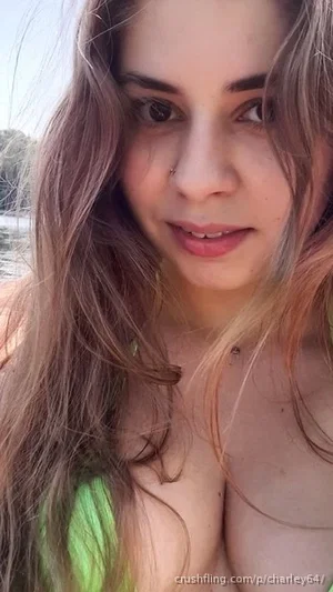Woman with long brown hair in green top, outdoors near water.