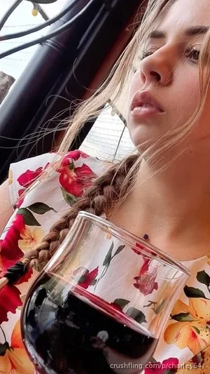 Woman with braided hair in floral top holding glass of dark liquid, indoor setting.