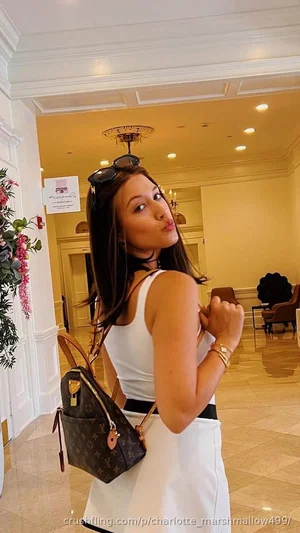 Woman in white tank top and skirt posing in a hotel lobby with a designer bag.