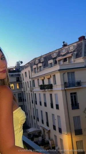 Woman in yellow strapless top on balcony overlooking city buildings at dusk.