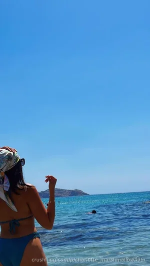 Woman in blue bikini and patterned headscarf standing at beach, facing ocean.
