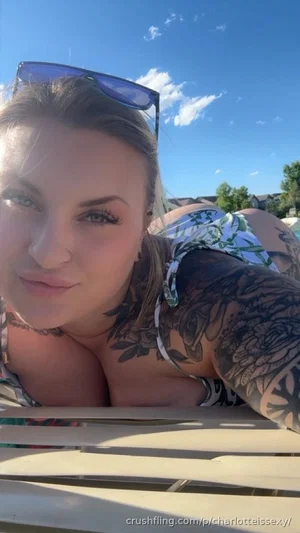 Woman with tattoos in floral top lying on bench outdoors under blue sky.