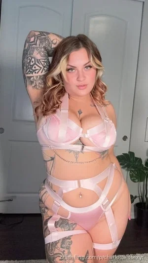 Woman with tattoos in pink lingerie posing indoors near a door.