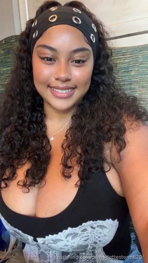 Woman with curly hair wearing black lace top, smiling in indoor setting.