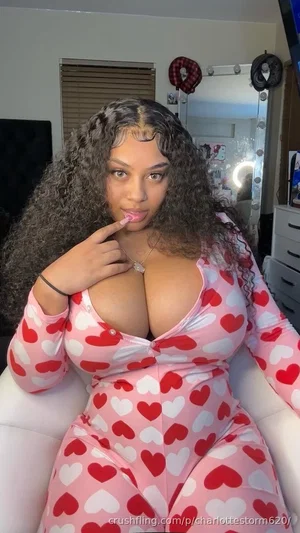 Woman with curly hair in pink heart-patterned bodysuit posing indoors.