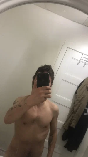 Shirtless man with tattoos taking mirror selfie in indoor setting.